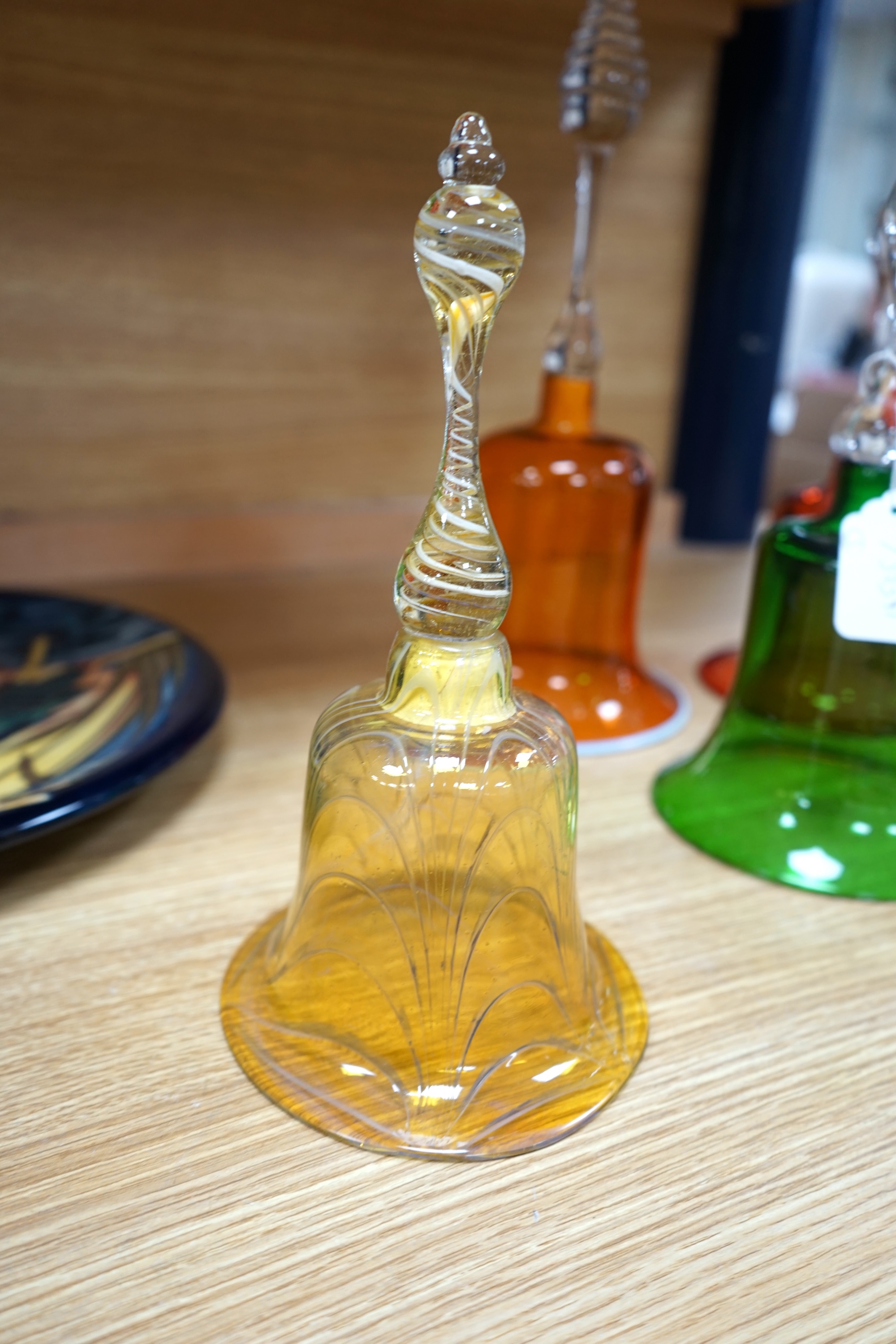 Five hand bells comprising an amber glass example with twist handle, two orange and two green glass hand bells, largest 36cm high. Condition - some repairs